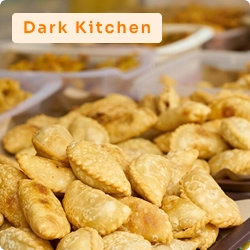 Produção de salgados assados ou fritos organizada em bandejas plásticas, representando operação de cozinha oculta (dark kitchen).